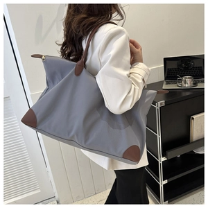 Bolso de viaje grande de nailon gris con asas de cuero marrón llevado al hombro.