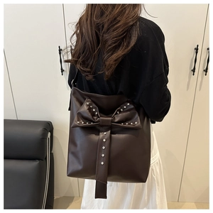 Detail of a dark brown shoulder bag featuring a large bow with rhinestone and stud accents