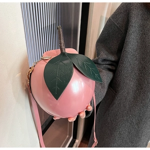 Gros plan d'un sac bandoulière rose en forme de pêche avec détails de feuilles