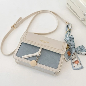 Close-up of contrast color crossbody bag with silk scarf handle and golden metal charm