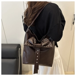 Detail of dark brown leather tote bag with oversized bow and silver metal studs