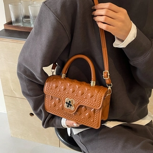 Detailed close-up of brown quilted handbag with clover metal clasp and woven texture