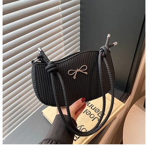 Close-up of black woven shoulder bag with silver metal bow and thick rope strap details
