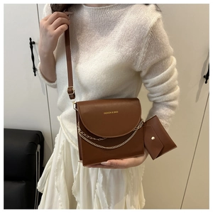 Détail d'un sac bandoulière marron avec chaîne dorée et petite pochette assortie