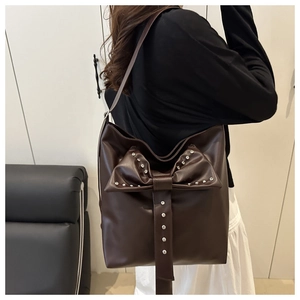 Detail of dark brown leather tote with large bow and silver stud accents on shoulder strap