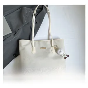 Dettaglio borsa tote intrecciata bianco crema con placca dorata e pendente in peluche