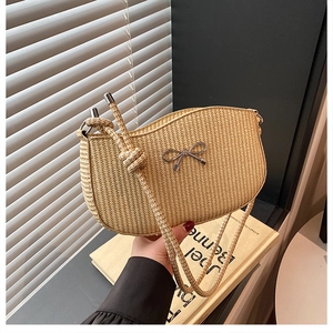 Close-up of beige woven straw shoulder bag featuring a silver metal bow and rope knot strap