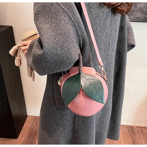 Sac à bandoulière rose en forme de pêche porté avec un long manteau gris élégant