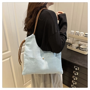 Detail of light blue canvas hobo bag with thick brown rope strap and metal rivets