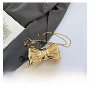 Detailed view of a shiny gold bow-shaped acrylic evening bag with a metal chain strap