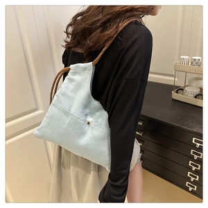 Detail of light blue denim tote bag with braided rope strap and metal rivet pocket