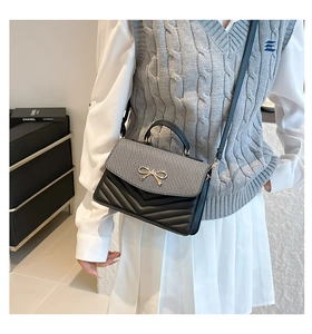 Detail of a chic flap bag featuring chevron quilting and a gold bow metal clasp