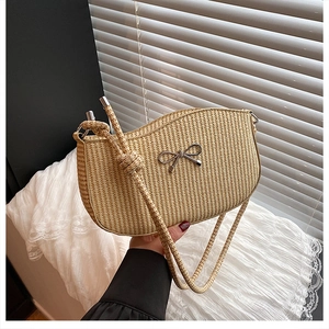 Detail of hand-woven beige straw bag featuring a silver metal bow and knotted strap design