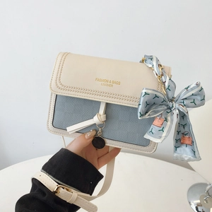 Close-up of contrast color leather shoulder bag with floral scarf and metal pendant