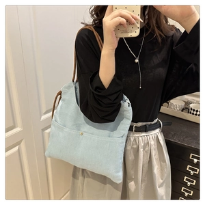 Detail of light blue denim tote with large front pocket and brown woven rope strap