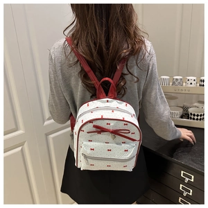 Detail view of mini white backpack with red bow print and heart pendant on a model