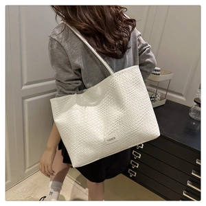 Detail of white tote bag with woven texture, fashion label and slim shoulder straps