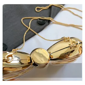 Detail of golden bow-shaped metal clutch with mirror finish and slim chain strap