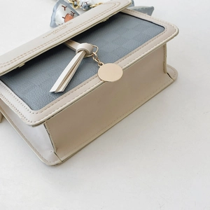 Detail of crossbody bag with grey textured flap, beige tassels, and floral scarf accent
