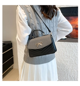 Detail of crossbody bag featuring a golden bow buckle and V-shaped stitching textures