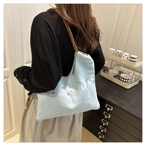 Detail of light blue denim tote bag with brown rope handles worn over the shoulder