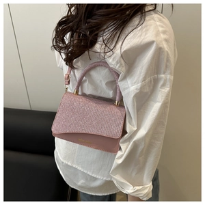 Vista laterale della borsa rosa glitterata con finiture dorate su camicia bianca
