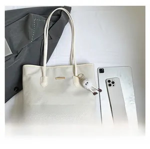 Dettaglio borsa tote beige intrecciata con ciondolo e iPad per confronto dimensioni