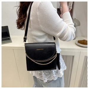 Détail du sac bandoulière en similicuir noir avec chaîne dorée porté par un mannequin