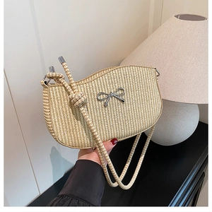 Detail of woven beige underarm bag featuring a silver metal bow accent and rope strap