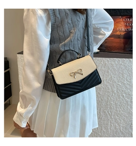 Detail view of a two-tone square handbag with gold bow lock and V-quilted leather texture