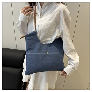 Detailed close-up of blue denim tote bag with white stitching and leather strap