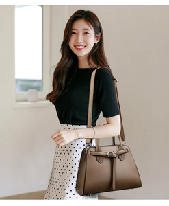 Detail of a brown trapezoidal faux leather handbag with buckle strap and detachable handle