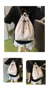 Detail of cream drawstring backpack featuring black bow embroidery and leather base