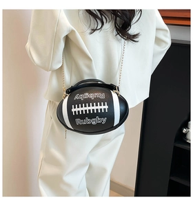 Detail view of a stylish black rugby-shaped crossbody bag with gold chain strap on model
