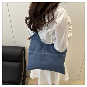 Detail of blue denim tote bag featuring white stitching and a round gold metal clasp
