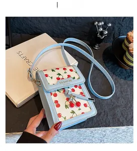 Close-up of light blue phone bag featuring red cherry prints and matching cherry charm