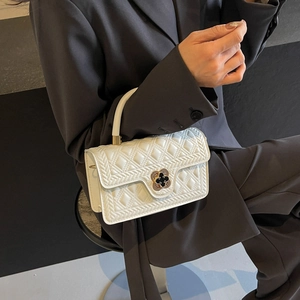 Detail of white quilted crossbody bag featuring a clover-shaped gold metal clasp lock