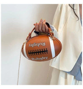 Detailed view of rugby-shaped brown leather handbag with gold chain strap held by model