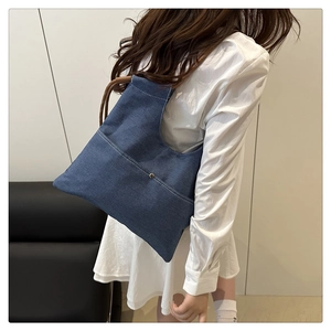 Detail of blue denim tote bag with white stitching and brown braided shoulder strap