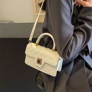 Detail of white quilted handbag featuring a golden clover-shaped metal clasp and flap