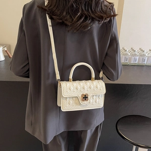 Detail of white quilted handbag featuring a gold clover twist lock and leather handle