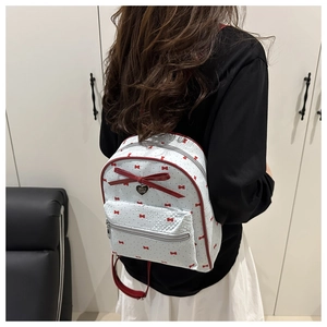 Close-up of small white leather backpack with red bow, heart prints, and gold pendant