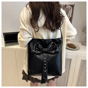 Close-up of black PU shoulder bag with bow and silver rivets on a person's shoulder