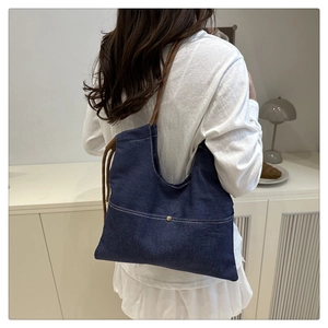 Detail of dark blue denim tote bag with brown rope handle shown on a shoulder