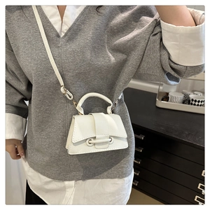 Macro detail of white trapezoid crossbody bag with lychee texture and buckle detail