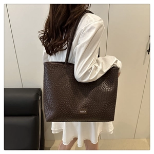 Detailed close-up of dark brown tote bag with woven texture and fashion metal plate