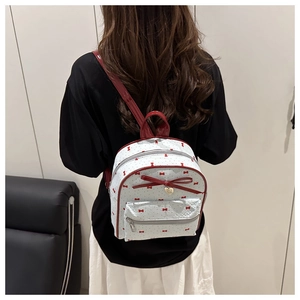 Close-up of a mini white backpack with red bows, gold heart pendant and shiny straps