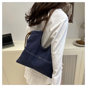 Detail of dark blue denim tote bag with white stitching and woven rope handle on model