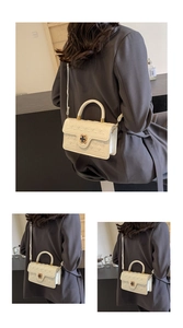 Detailed view of white quilted handbag with golden clover clasp and top handle grip