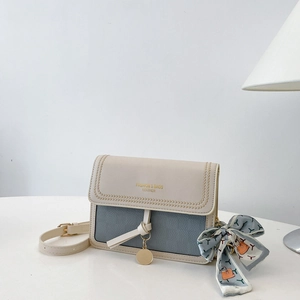 Detail view of contrast stitching and silk scarf on a beige and blue leather crossbody bag